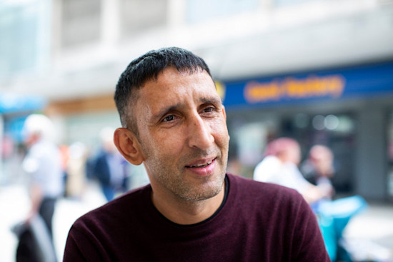 Paddy looking off camera with a blurry shot of shops behind him