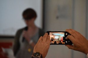 Someone taking a photo on their phone of a speaker at an event.