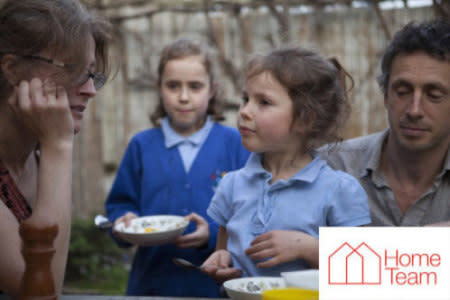Two young children eating bowls of cereal with their family