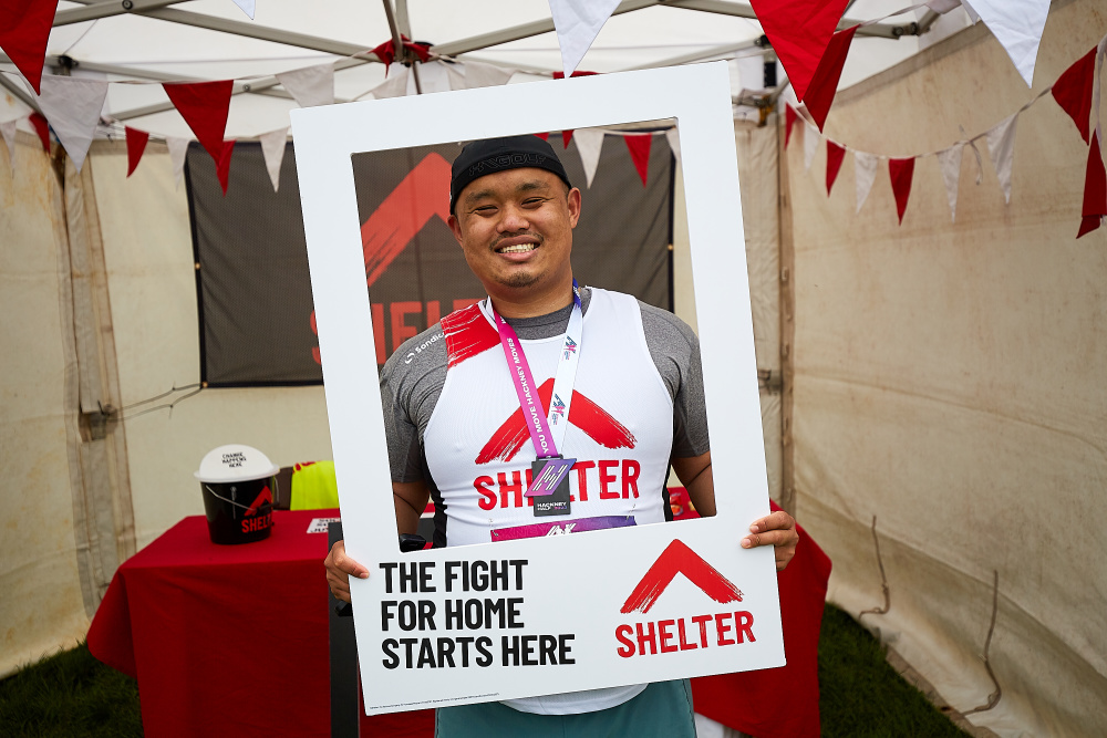 A Hackney Half marathon runner stands smiling in the frame of a Shelter prop 