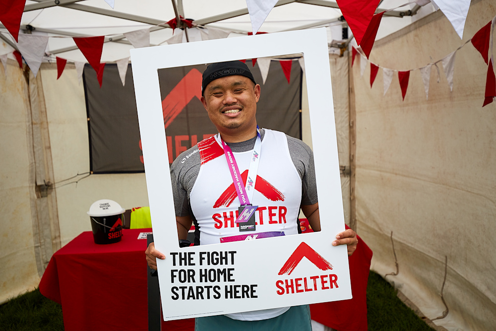 A Hackney Half marathon runner stands smiling in the frame of a Shelter prop