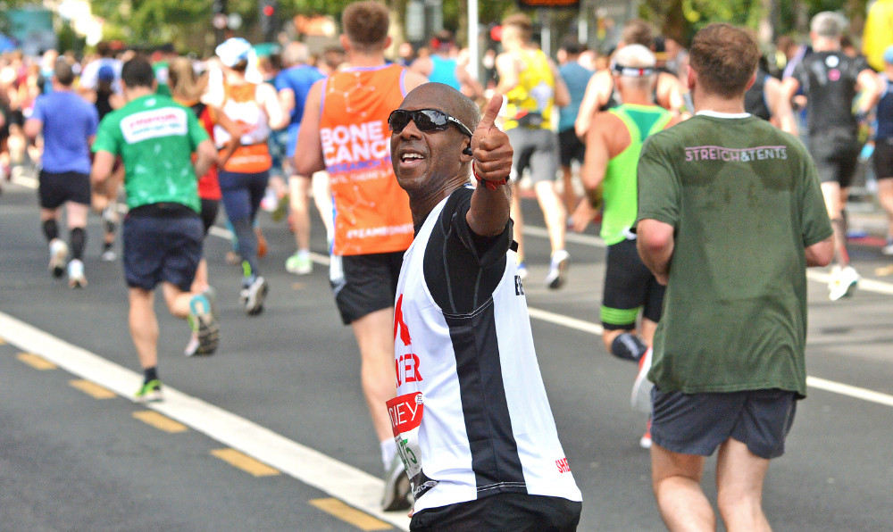 A man raises his thump up triumphantly while running the Hackney Half
