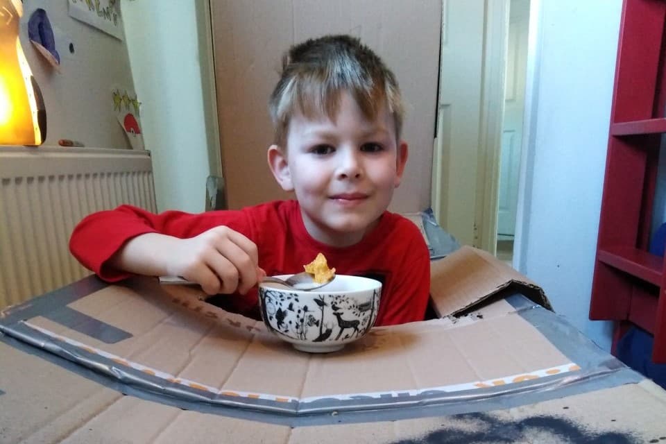 Laurie smiles into the camera as he sits with his cardboard box
