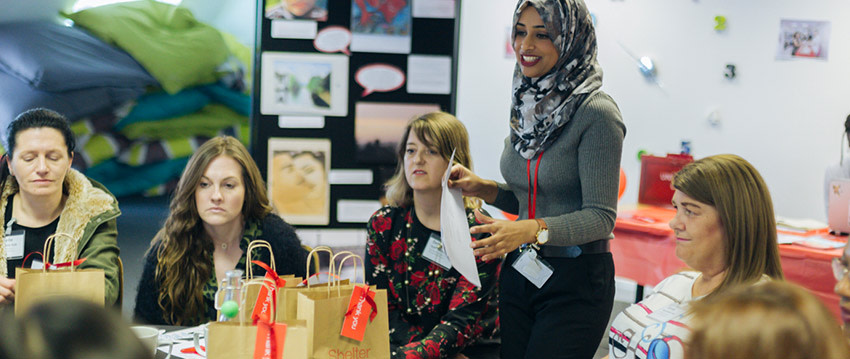 Five women, one standing wearing a hijab and four seated, at a workshop meeting.