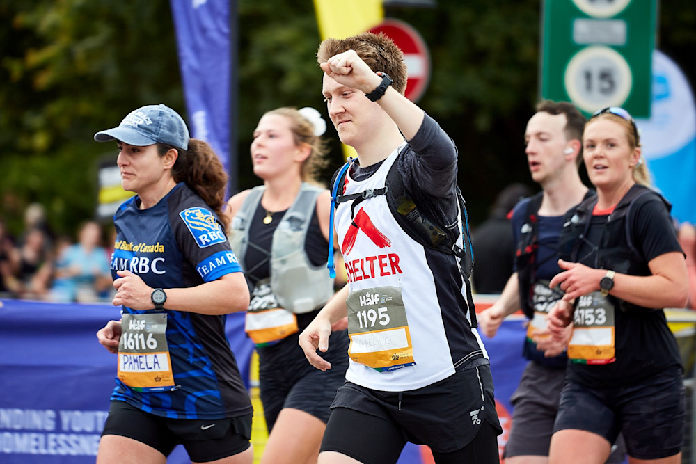 A runner in a Shelter vest passes the cheer point of his race and punches the air in celebration.