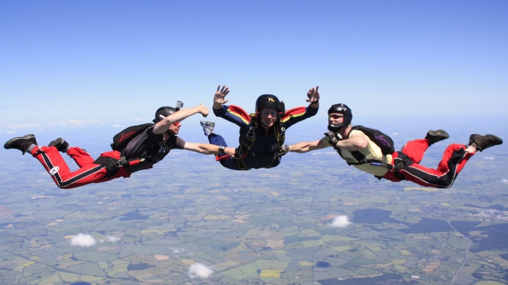 A group of three skydivers are seen lying forward in the air during a jump