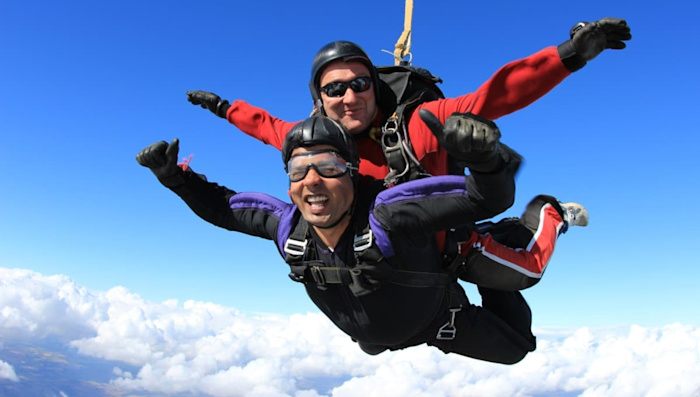 Two smiling people parachute through the sky