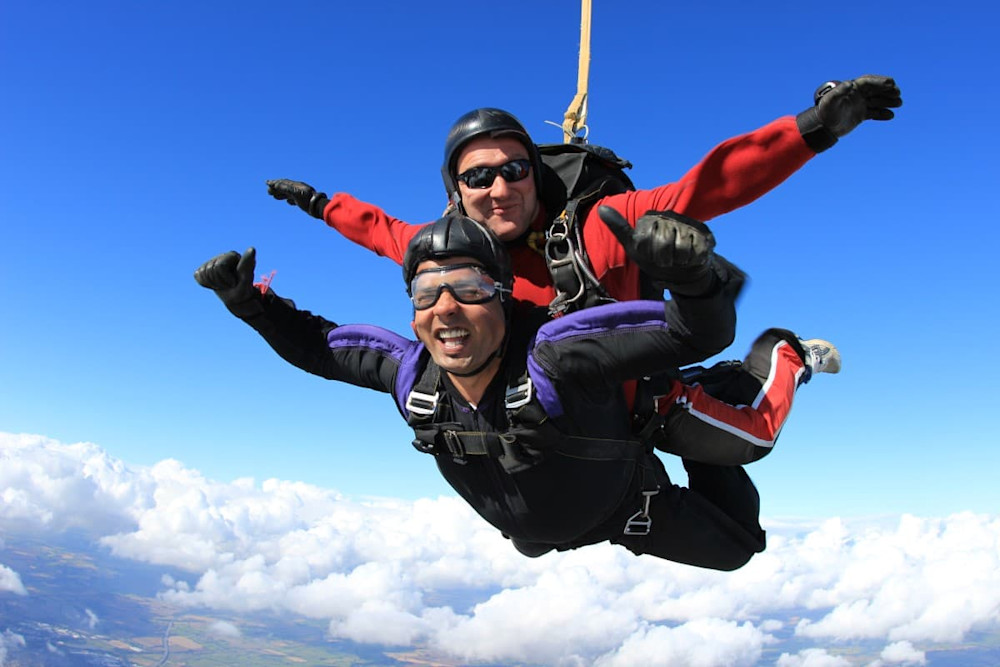 Two smiling people parachute through the sky