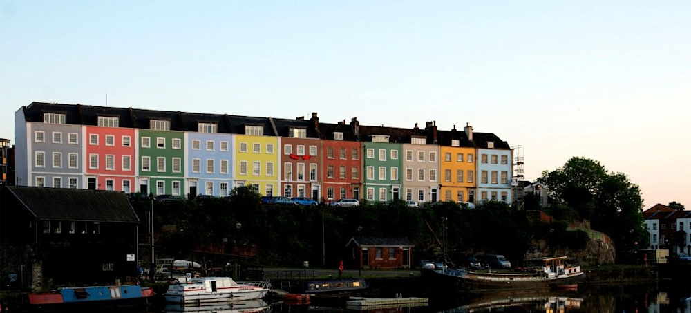 A row of multicoloured terraced houses next to a river.