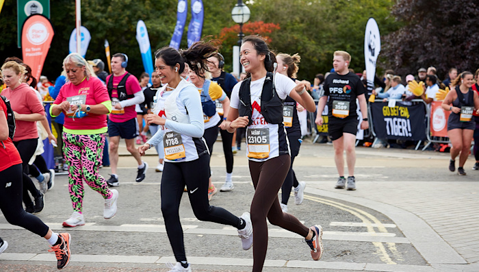 Two women in Shelter vests smile as they run past the cheer point of the Royal Parks Half Marathon.