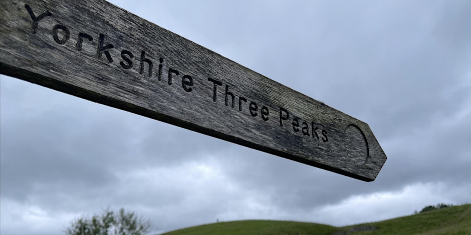 A wooden sign in the countryside that reads 'Yorkshire Three Peaks' and points along a pathway.