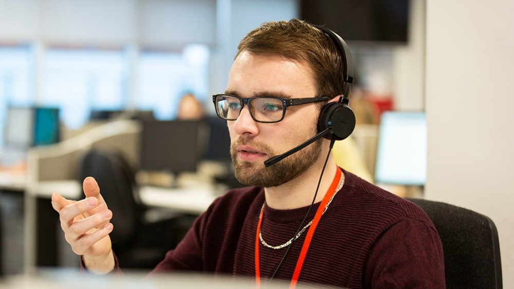 Helpline adviser Adam is seen across the office speaking into a headset