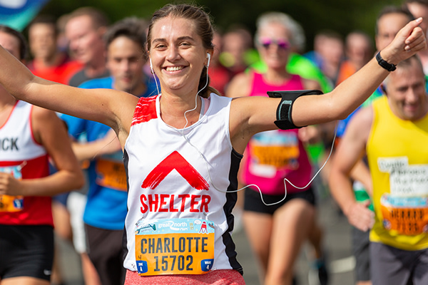 A woman wearing a Shelter vest is smiling as she runs alongside others in the Great North Run