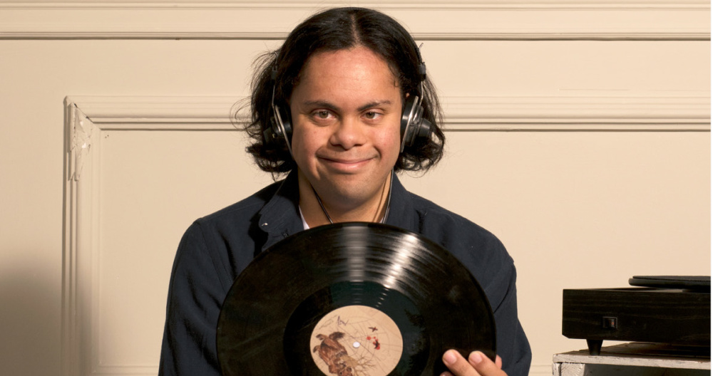 A young man smiles as he holds a vinyl record 