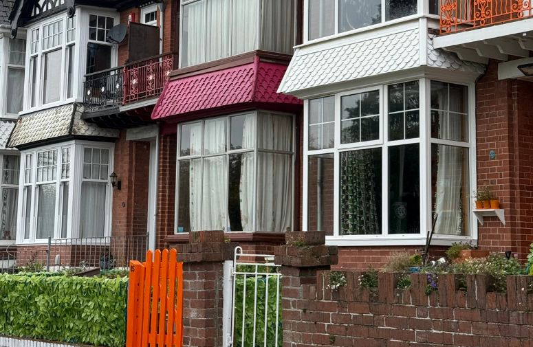 Row of Victorian style housing with pink bay tiling on bay window and bright orange gate