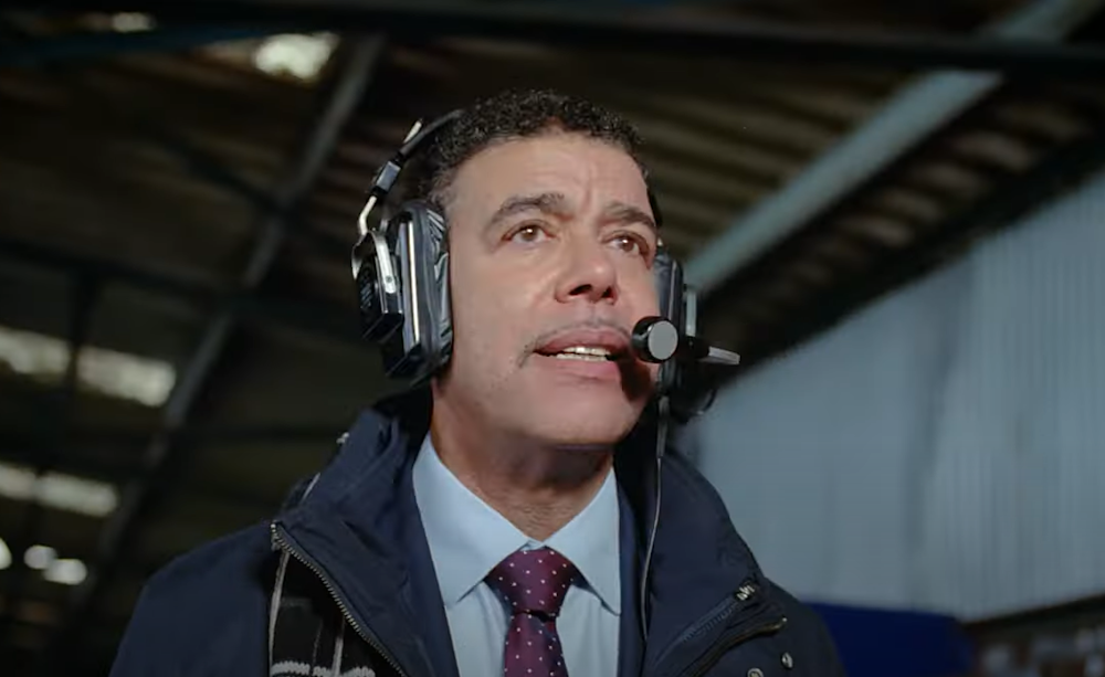 Chris Kamara wearing a headset with microphone in a stadium
