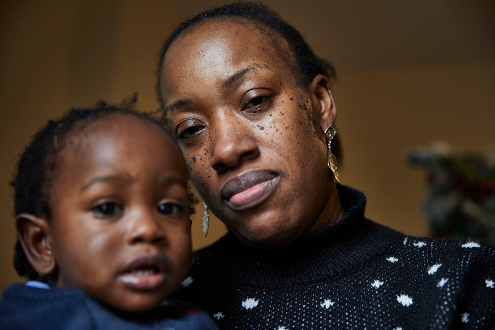A Black woman holding her baby and looking at the camera