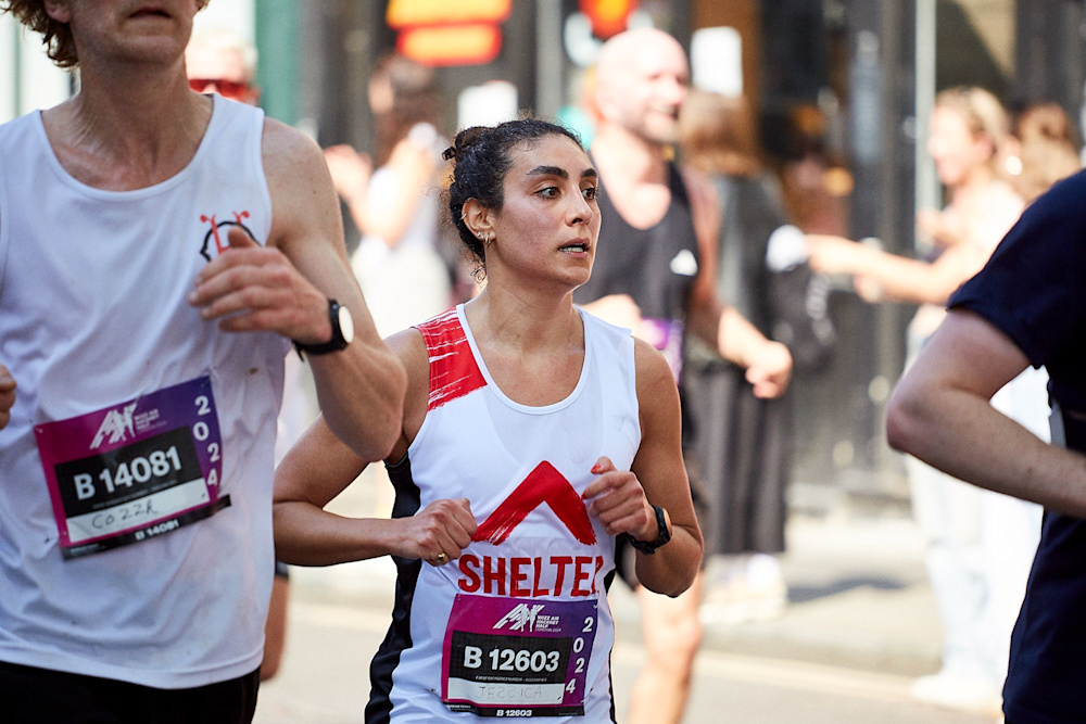 A woman running in a Shelter vest, surrounded by other race participants. She looks focused and determined.