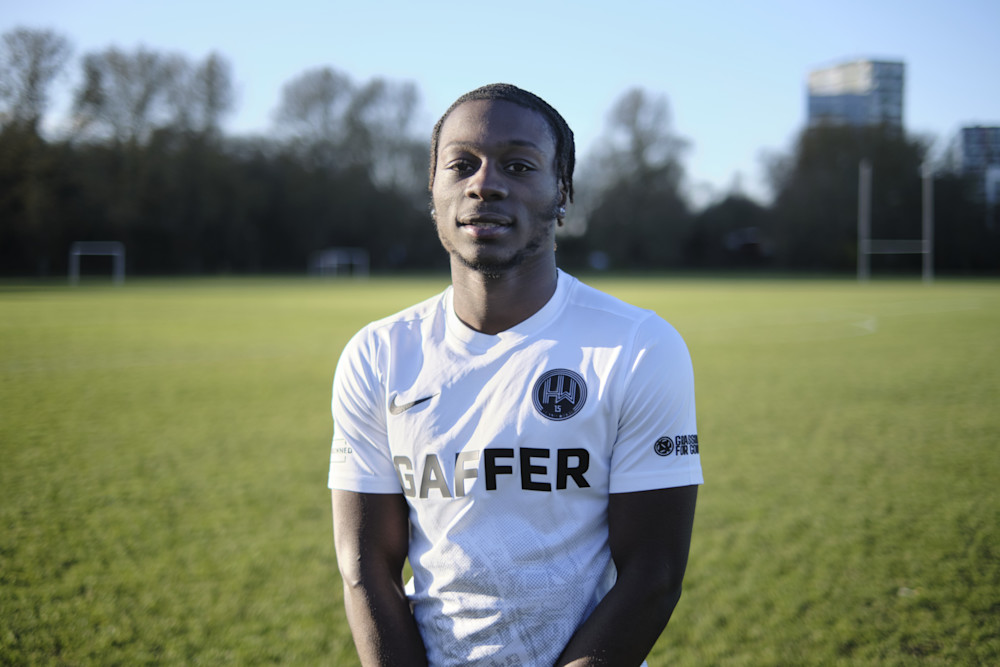 A man on a pitch wearing a white Hackeny Wick FC shirt