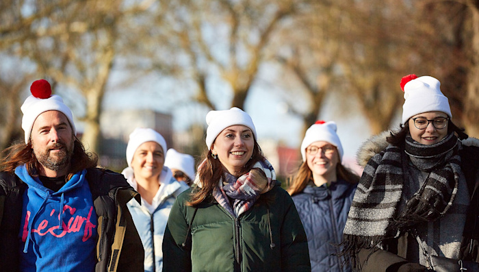 A group of five people walking in a park, wearing coats and bobble hats.