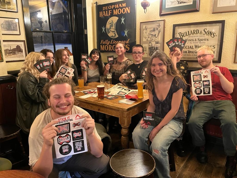 NRC members sit together inside a pub. They hold up NRC posters and flyers.