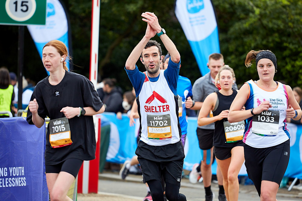 A runner in a Shelter vest claps his hands overhead as he passes the cheer point of his race.
