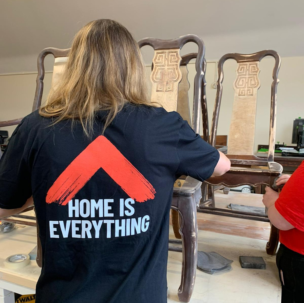 A person wearing a Shelter t-shirt furnishing furniture