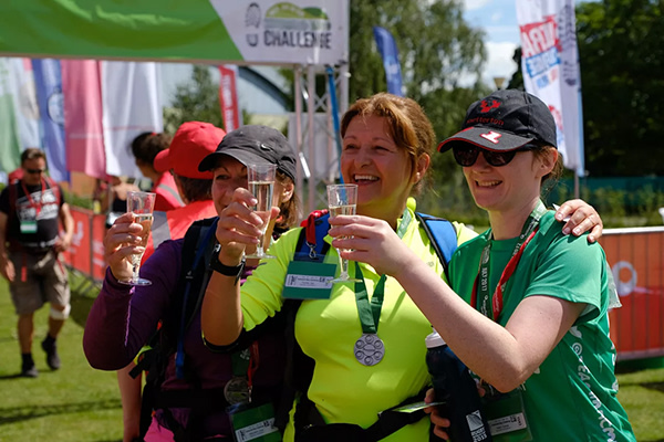 Three women holding up glasses of sparkling wine and smiling as they stand at the finish line