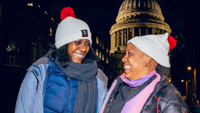 Two women wearing Shelter bobble hats take part in the Walk for Home London event. They are both smiling.