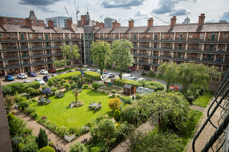 A view looking down on two square blocks of social housing, with cars parked around the edge and a green in the middle. City buildings are visible in the background.
