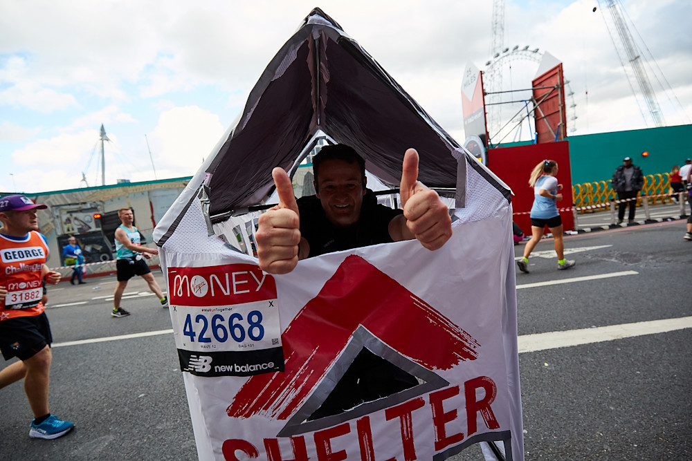 A man is running the London Marathon in a fabric house with the shelter logo on it