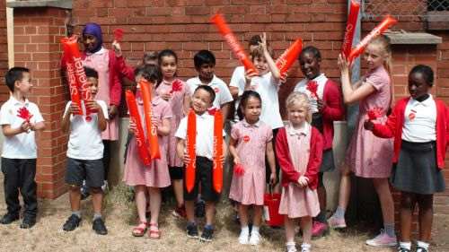 A group of school children in uniforms outside waving Shelter balloons