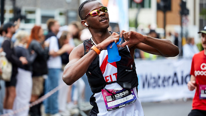 A runner wearing a Shelter vest and sunglasses makes a heart shape with his hands as he passes the cheer point of the Hackney Half Marathon.