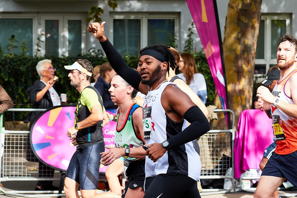 A male marathon runner raises his thumb in response to the crowd whilst running 