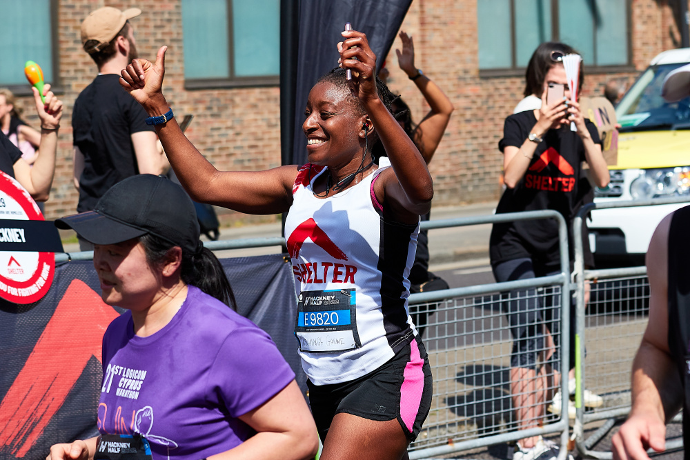 A Black woman running a race in a Shelter vest