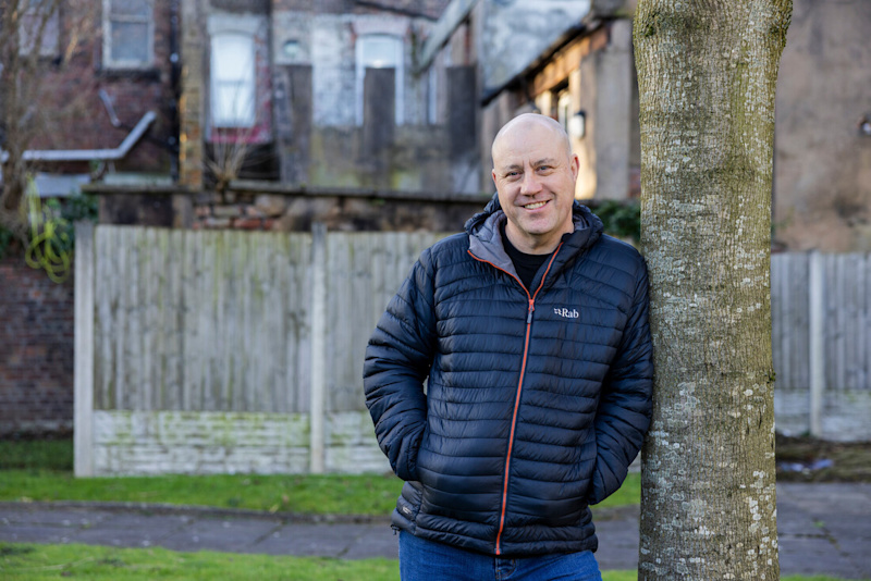 Photo of Ray, a white-man of middle age standing against a tree and smiling.