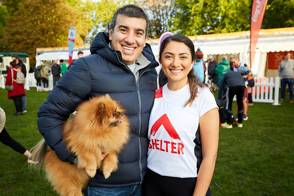 A woman in a Shelter running top stands with her supporter and a cute fluffy Pomeranian dog before the race starts.