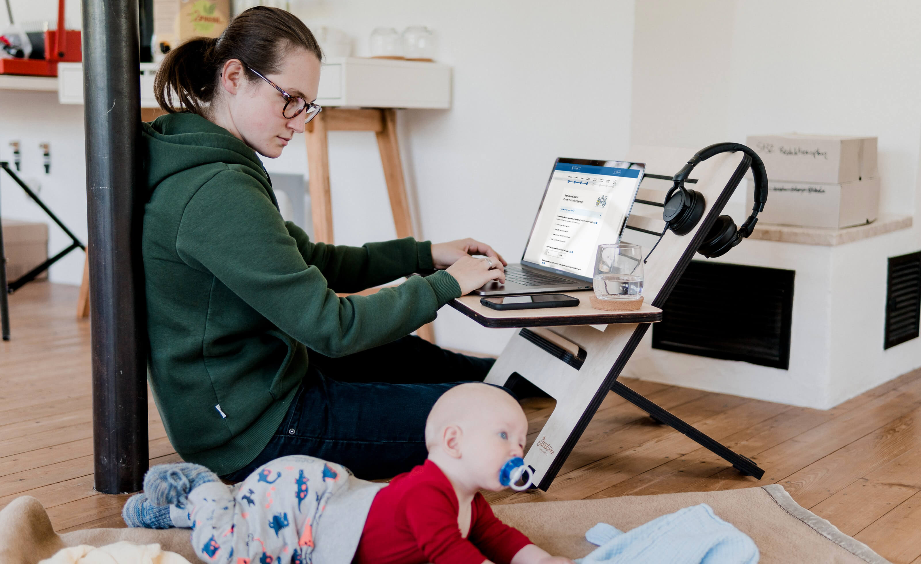 A mother completes the eligibility guide on a laptop with her baby on a rug beside her.
