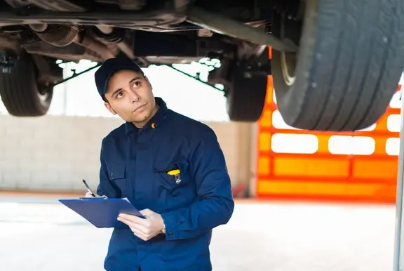 Male car mechanic checking under car