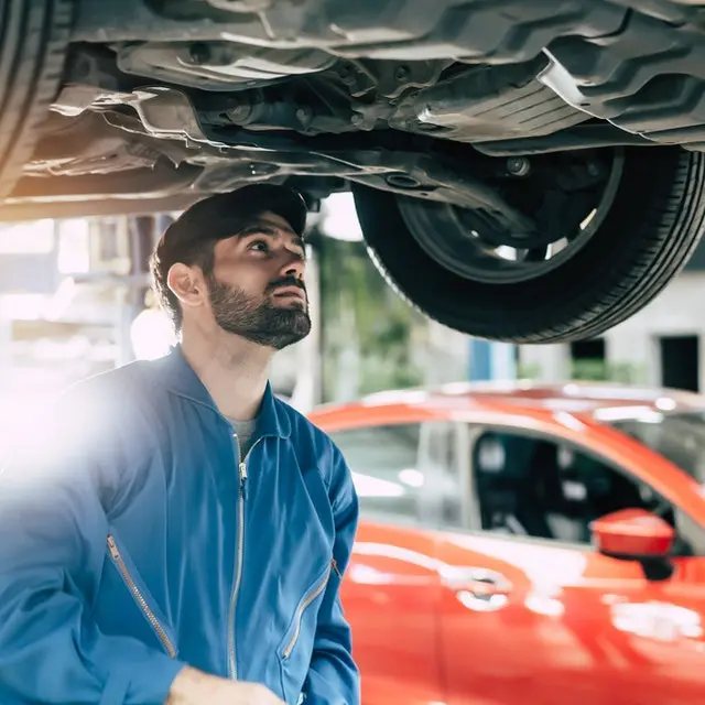Male car mechanic checking under car