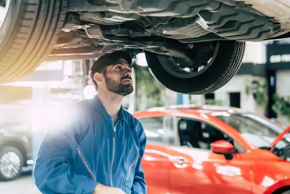 Male car mechanic checking under car