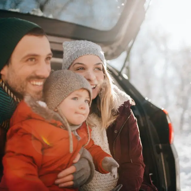 Family sat on a car bumper looking out at the snow