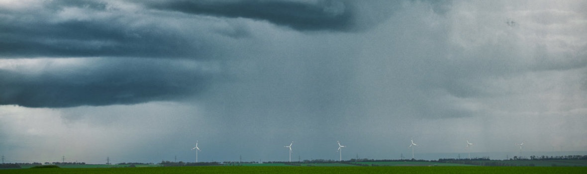 Windräder auf grüner Wiese, unter dunklen, stürmischen Wolken.