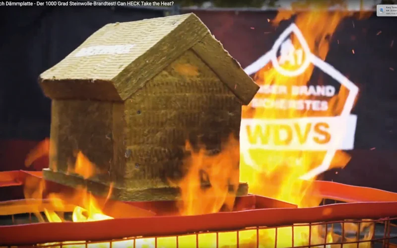 Haus aus Dämmstoff steht auf brennendem Gitter und symbolisiert Brandschutz