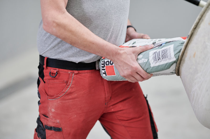 Ein Mann füllt einen Sack Baumit Beton in einen Betonmischer.