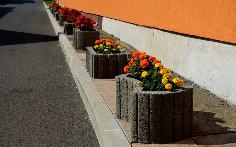 Schalungssteine gefüllt mit bunten Blumen stehen am Rand eines Parkplatzes