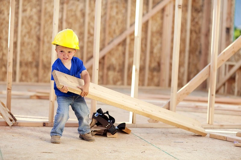 kleines Kind mit Holz in der Hand auf einer Baustelle
