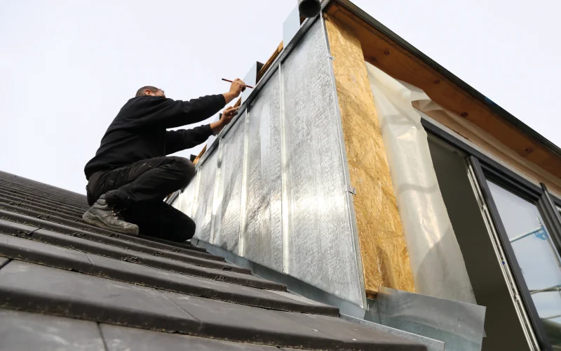 Arbeiter sitzt auf Steildach und bearbeitet Dämmung am Fenster