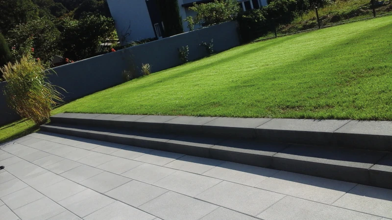 Rasen mit zwei Stufen hinter einer Terrasse mit hellgrauen Terrassenplatten