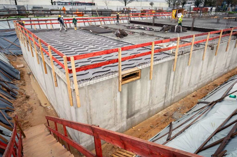 Betonrohbau mit Bewehrung für Decke, Baustelle mit Absturzsicherung und Arbeiter.